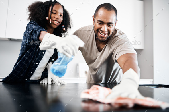 Shot of a young girl helping her father clean the kitchen counter at home