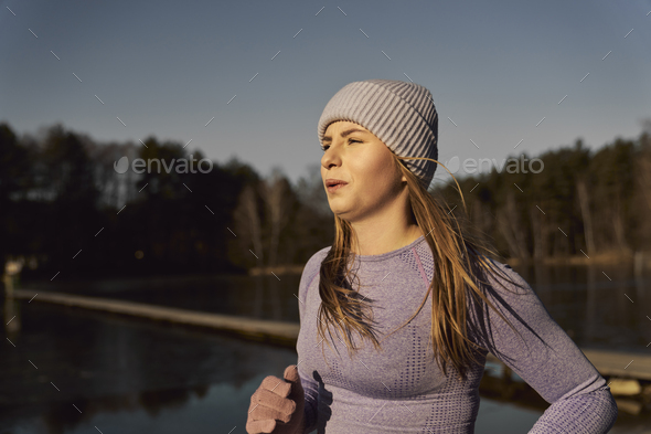 Side view of adult caucasian woman jogging on beach by the lake in the winter - Stock Photo - Images