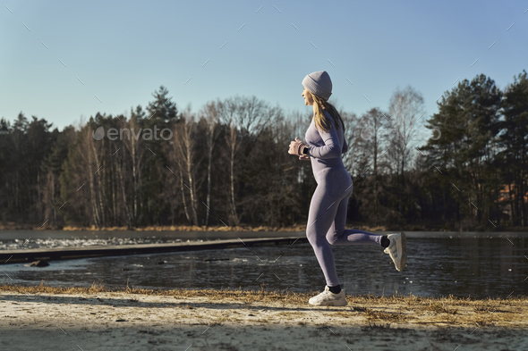 Full length of adult caucasian woman jogging on beach by the lake in the winter - Stock Photo - Images