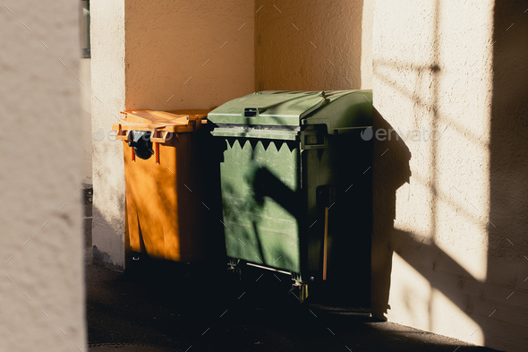 The yellow and green trash cans stand in the archway of the house. The sun is shining brightly