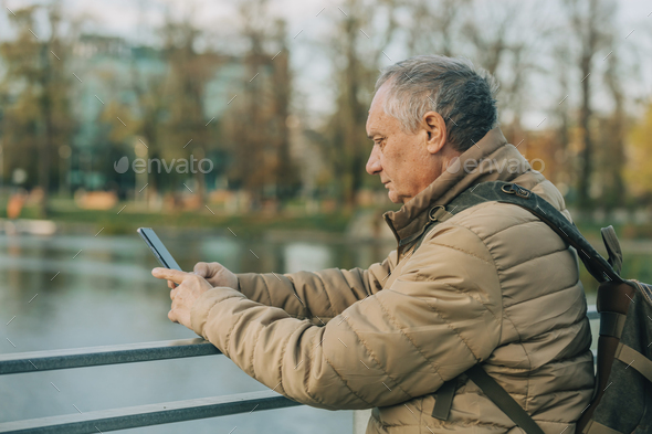 Senior male with mobile phone stands near river in Wroclaw, Poland - Stock Photo - Images