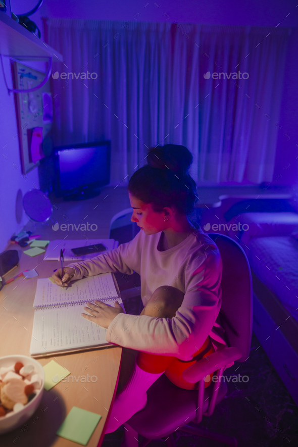 Girl studying in her room decorated with LED lights Stock Photo by