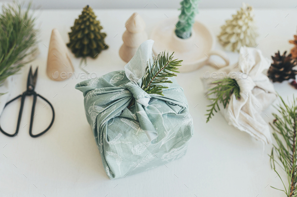 Stylish christmas gift wrapped in fabric on rustic table with