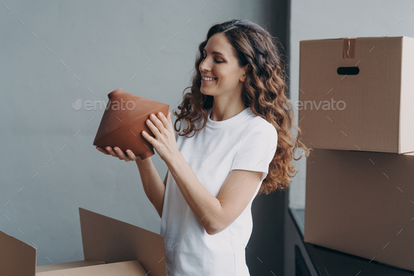 Relocation and delivery service concept. Happy girl unpacking cardboard boxes and holding the vase. - Stock Photo - Images