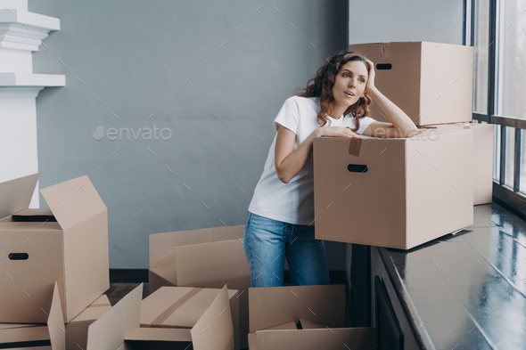 Woman unpacking boxes and dreaming. Enjoying view looking at the window in new apartment. - Stock Photo - Images