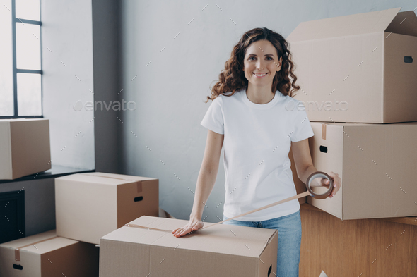 European lady is wrapping cardboard boxes with packing tape. Moving service worker. - Stock Photo - Images