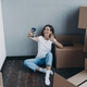 Happy young spanish woman in jeans and white t-shirt unpacking boxes having video call on phone. - PhotoDune Item for Sale