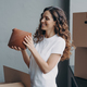 Relocation and delivery service concept. Happy girl unpacking cardboard boxes and holding the vase. - PhotoDune Item for Sale