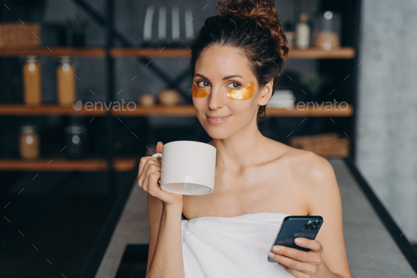 European girl drinks coffee and texting on smartphone and relaxing. Evening body care routine.