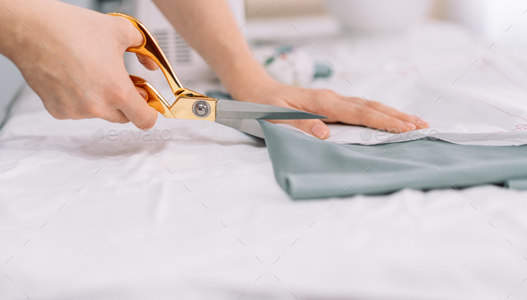 Lady cuts out patterns with scissors from a piece of fabric in front of the sewing equipment - Stock Photo - Images