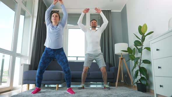 Caucasian Couple is Doing Jumping Jacks Exercise at Home in Cozy Bright Room Slow Motion alt