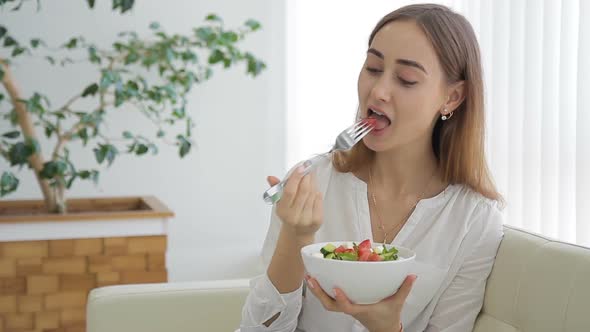 Happy Woman Relaxing on Sofa Eating Salad in Living Room alt