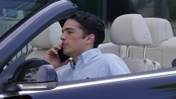 Young businessman getting into convertible car while talking on cell phone