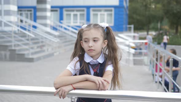 Portrait Shot of the Sad Little Girl in the School Uniform in the School Yard Against the Building