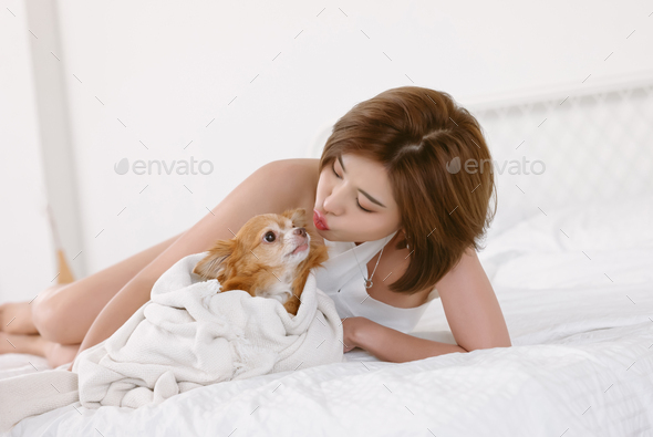 Beautiful Asian girl white off-shoulders clothes kissing with her lovely dog on bed in bedroom