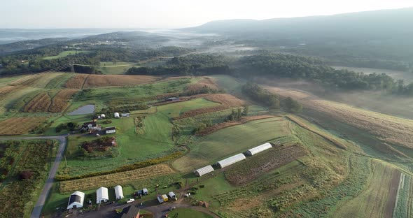 Aerial camera view of West Virginia countryside with farms, fields, mountains and fog settling in th alt