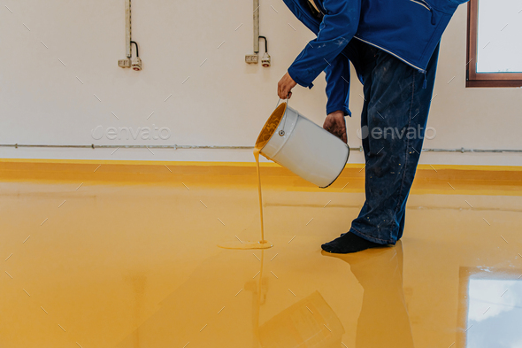 Worker, coating floor with self-leveling epoxy resin in industrial workshop.