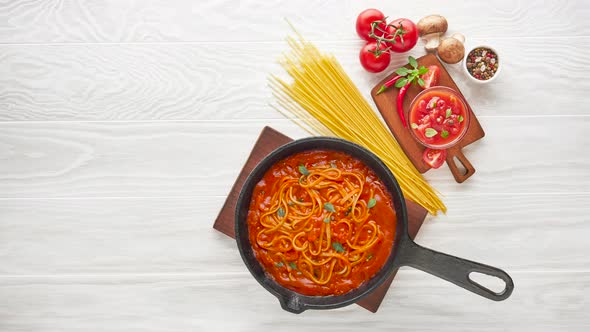 Boiling italian pasta with tomato sauce in cast iron pan served with red chili pepper, fresh basil