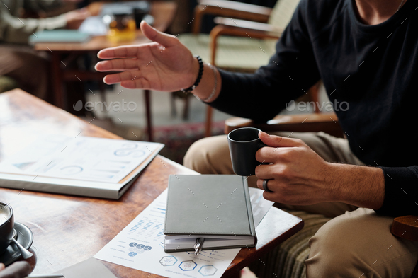 Hands of male economist with cup of tea during conversation with colleague - Stock Photo - Images