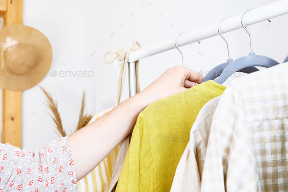 Woman takes linen dress on hanger from clothes rack.