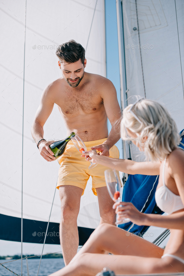 handsome shirtless man in swim trunks pouring champagne into glass of