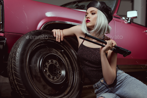 stylish blonde girl in beret leaning at car wheel and looking away while repairing car - Stock Photo - Images