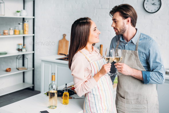 couple clinking with wineglasses in kitchen and looking at each other - Stock Photo - Images