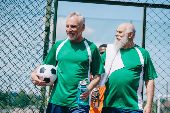 multicultural smiling elderly men with sportive water bottles and football ball
