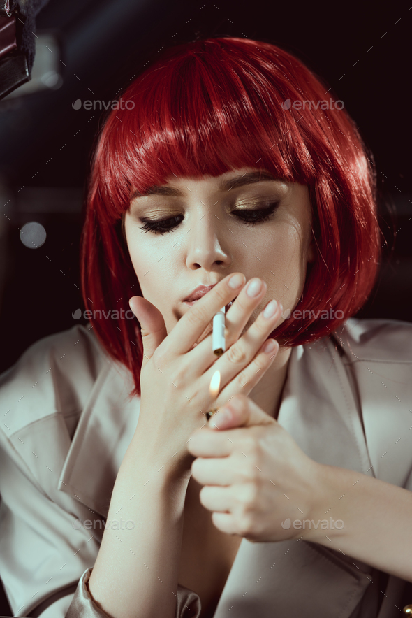 close up view of beautiful young woman in red wig smoking cigarette in car