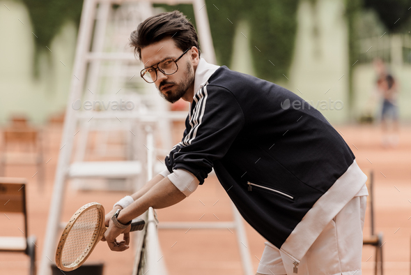 side view of handsome retro styled tennis player leaning on tennis net at court