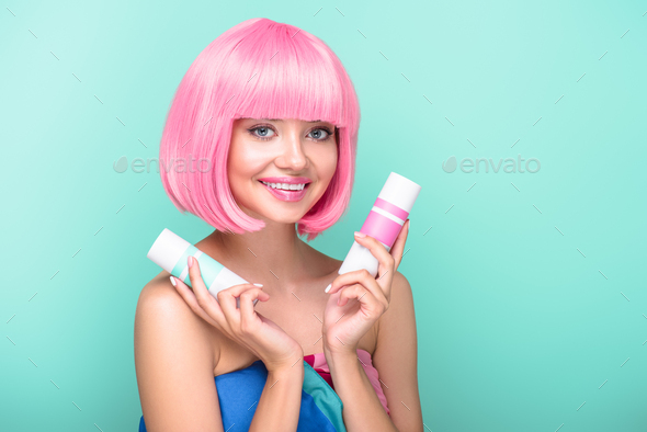 beautiful young woman with pink bob cut holding cans of coloring hair sprays isolated on turquoise