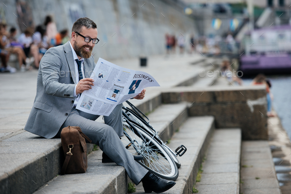 businessman in grey suit reading newspaper on stairs with bicycle