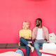 multiethnic young students working with laptop while sitting under red wall - PhotoDune Item for Sale