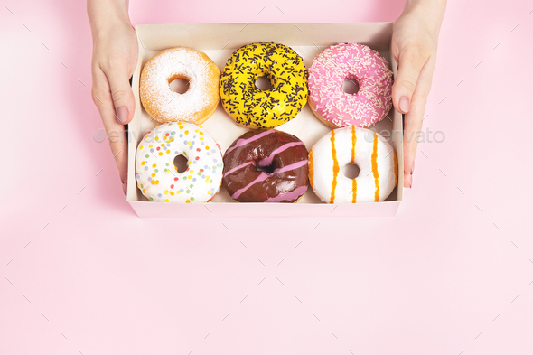 Hands is taking colored glazed donuts in donut box. Hands is grabbing different flavors doughnuts.