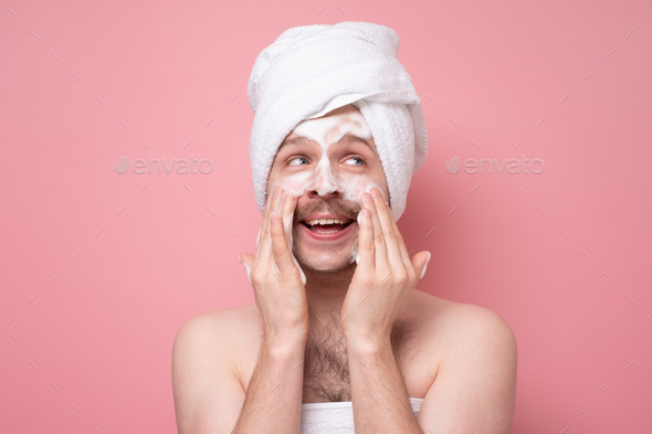 Surprised man washes face with cleanser and soap, has foam on skin