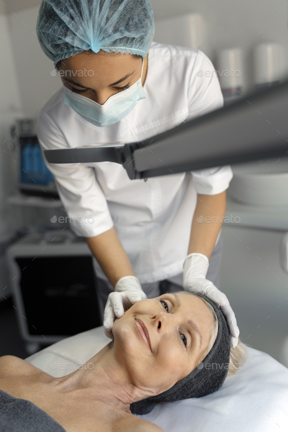 Vertical View Of Young Masseuse Massaging Senior Female Patient Face