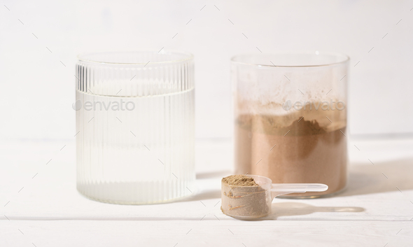 Whey protein powder with chocolate flavor in a spoon next to a glass of water. wellness product  - Stock Photo - Images