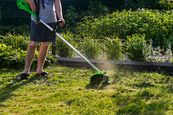 grass trimmer. A man mowing the grass. Outdoor view of young worker using a lawn trimmer mower cutti