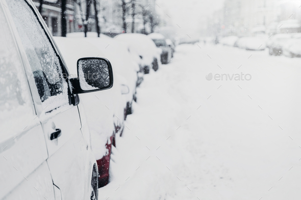 Many cars on winter road or in parking lot. Snowy city. Snowfall during winter