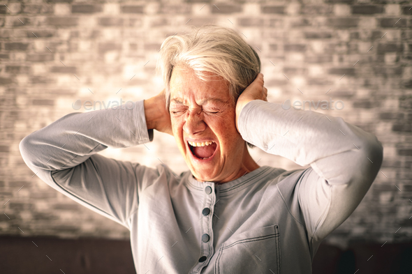 Desperate frustrated senior woman screaming in pain with hands on ears
