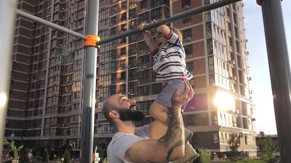 Happy Father and His 2Year Old Son Do Exercises on the Crossbar in the City Park alt