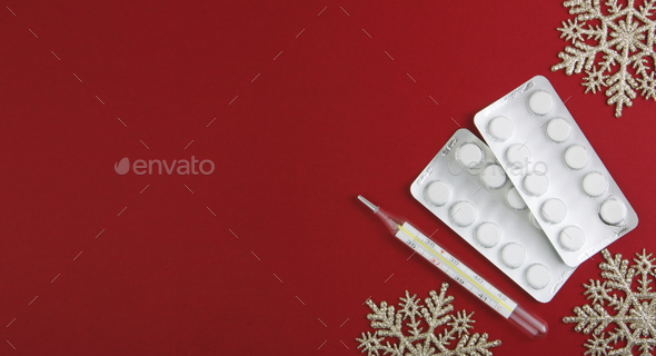 Medical Christmas background. Pills, blister and thermometer,on a red background with snowflakes