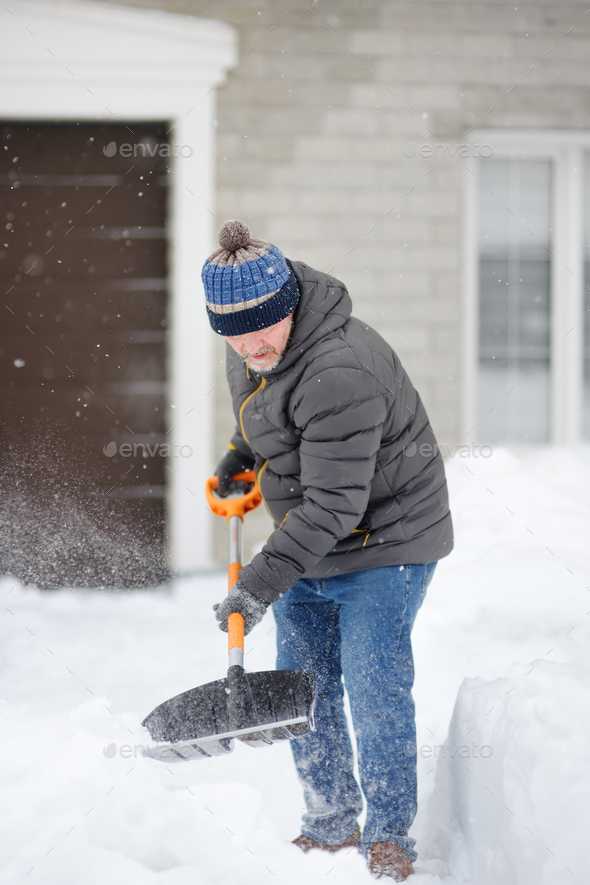 Mature man clean path near house from snow during strong blizzard.