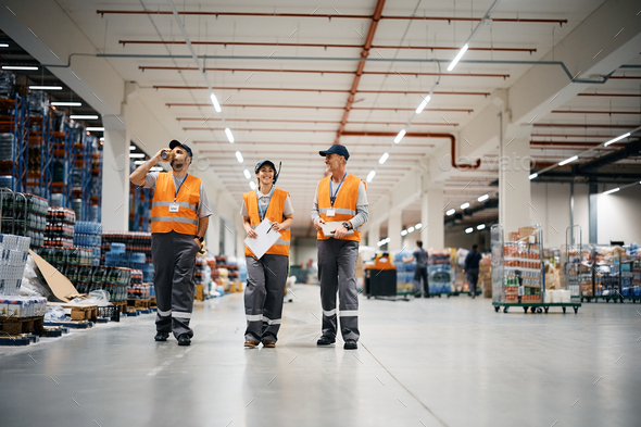 Group of happy warehouse workers walking through distribution storage compartment.