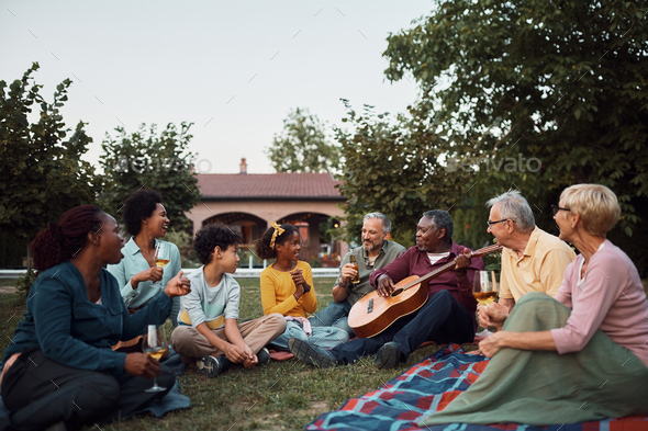 Happy multiracial extended family enjoying in drinks and acoustic music in the backyard.