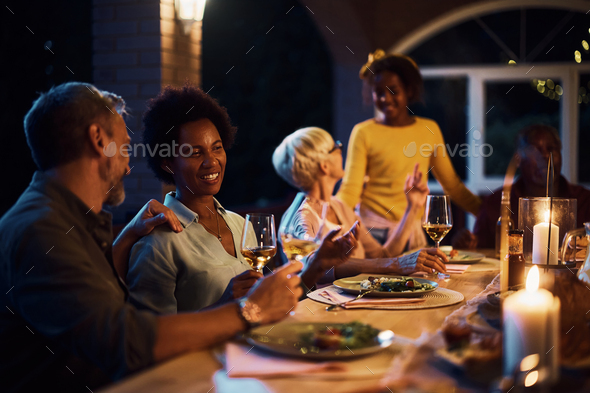 Happy black woman enjoying in wine and conversation with her husband during family dinner on patio.