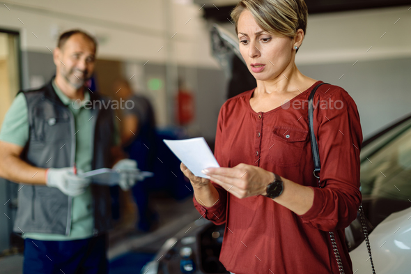 Mid adult woman feeling shocked with expense of car repairing in a workshop.