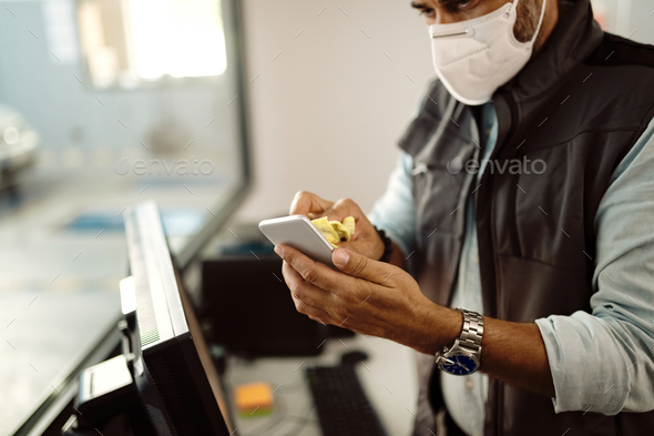 Close-up of auto mechanic disinfecting smart phone while working in the office at repair shop.