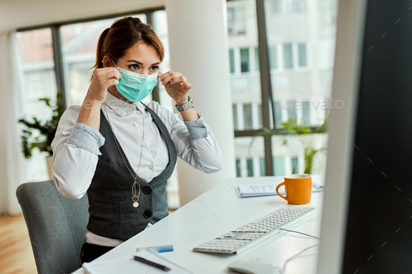 Young businesswoman putting on face mask while working in the office.