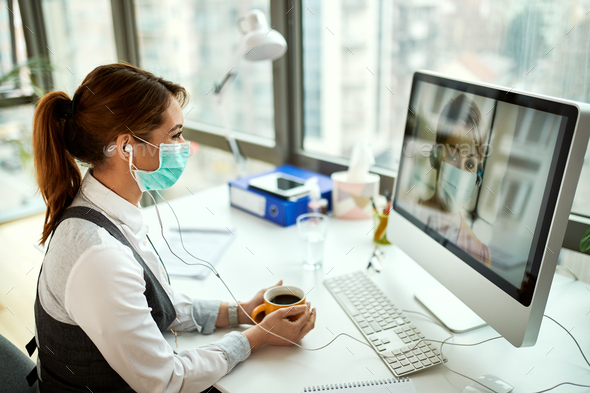 Businesswoman with face mask having video call with her colleague over desktop PC.